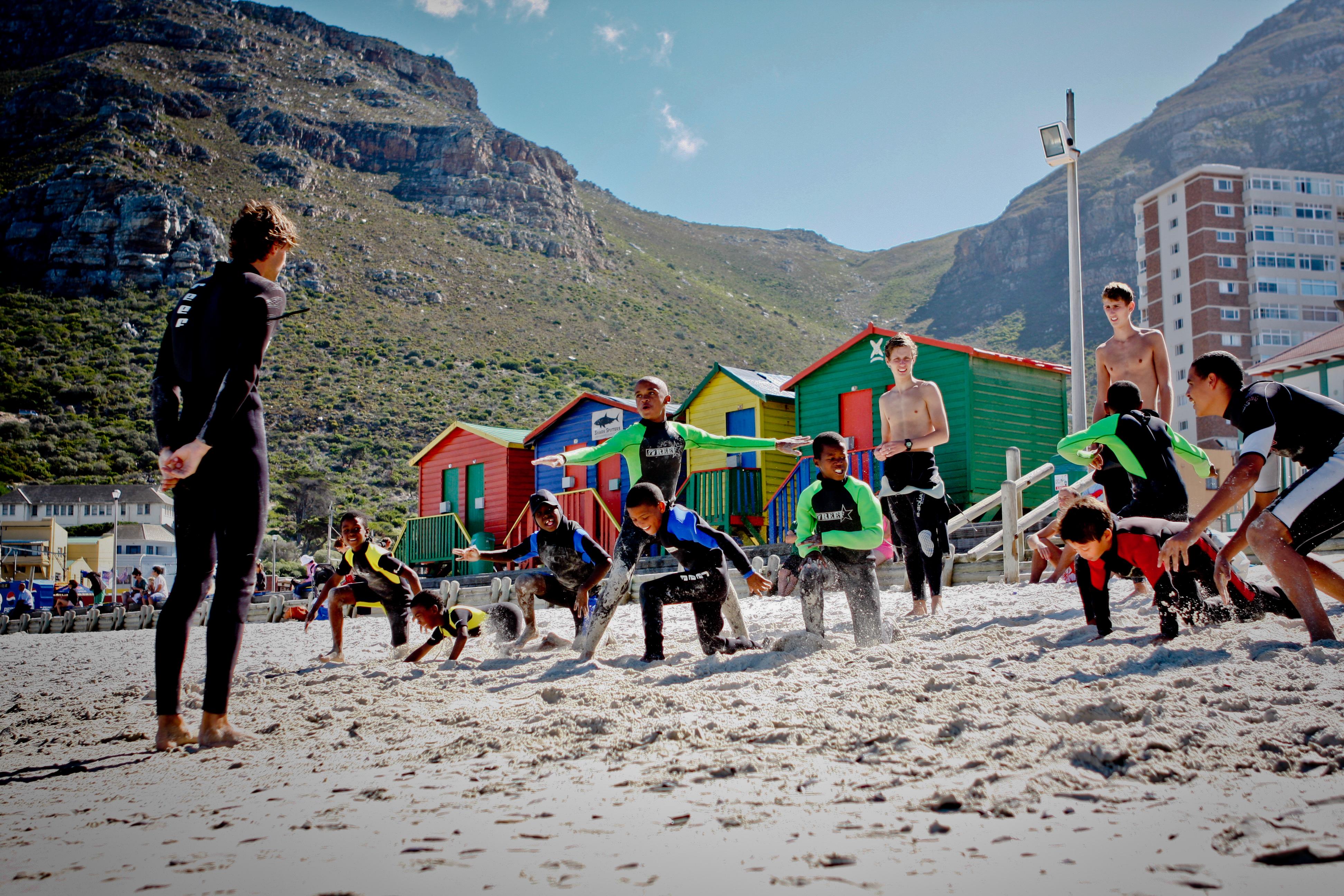 A Projects Abroad volunteer teaches surfing in South Africa by showing children how to stand on a surfboard Children learn to stand on their surfboards through volunteer surf coaching in South Africa